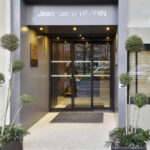 Sleek automatic sliding glass door at the entrance of Jean Luc TARTARIN restaurant, framed by a stylish metallic structure with warm lighting and decorative greenery.